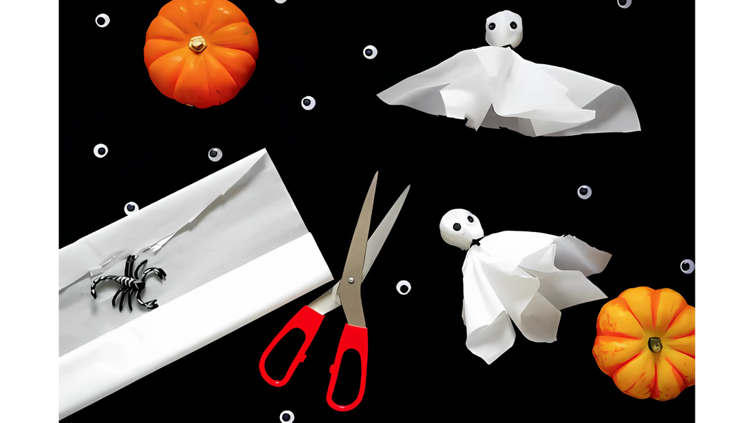 DIY Halloween craft with tissue paper ghosts, a pair of scissors, toy pumpkins, and a plastic scorpion placed on a black background.