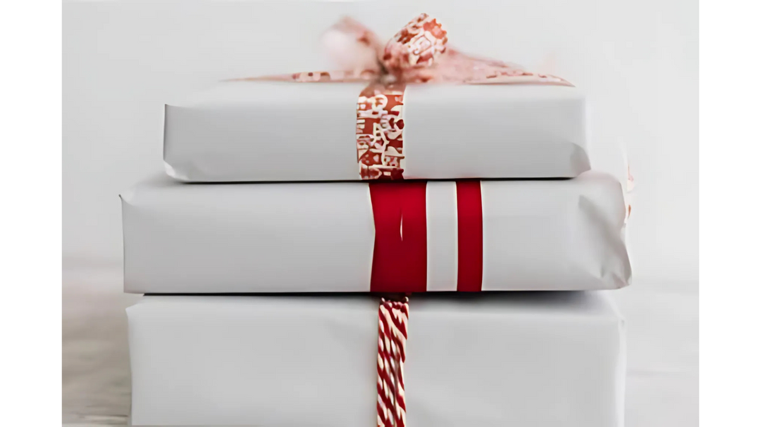 A stack of three neatly wrapped gifts in white paper with red and white decorative ribbons, creating a simple and festive presentation.