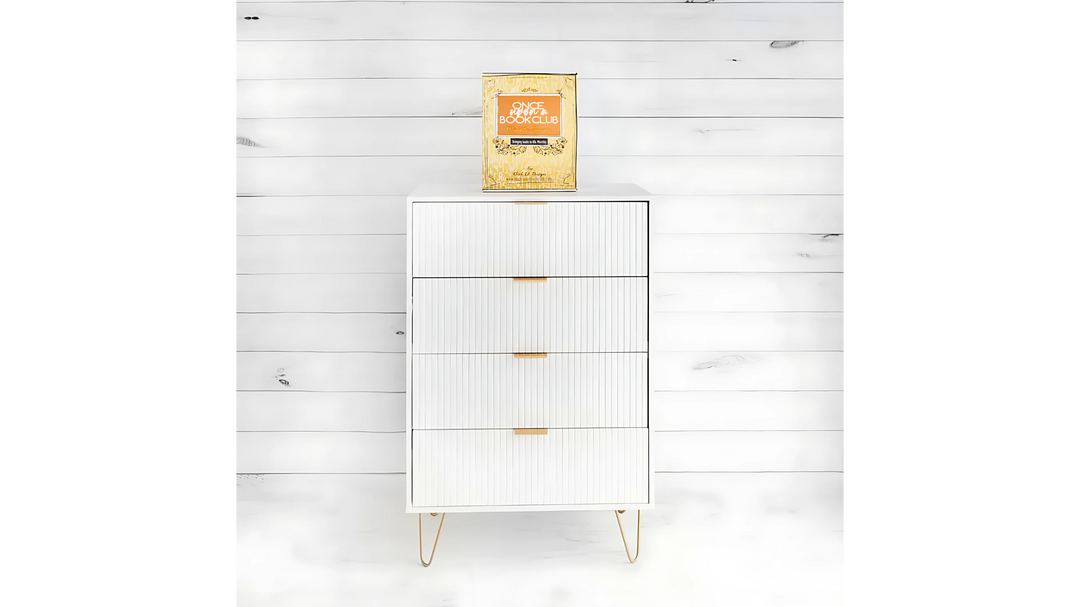 A golden "Once Upon a Book Club" box sits atop a modern white cabinet with gold handles, against a white shiplap background.