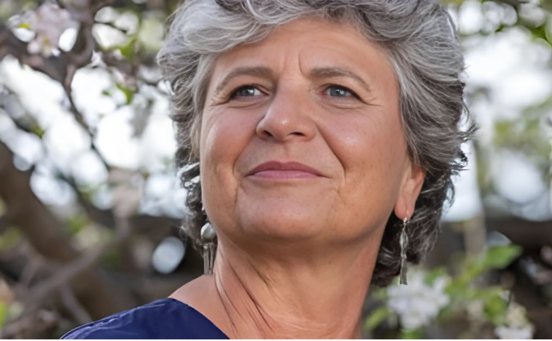 Donna Rowell, an author with short, curly gray hair, gazing confidently with a soft smile, set against a backdrop of blooming flowers.