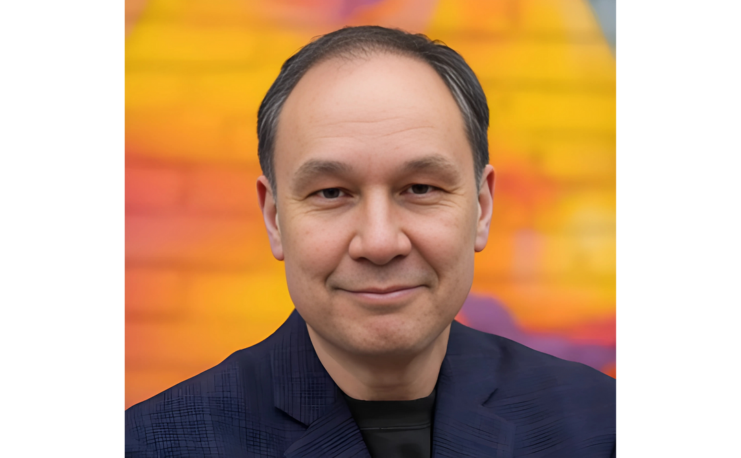 Portrait of Jamie Ford, an author, against a vibrant, colorful background. He is wearing a dark jacket and smiling gently at the camera.