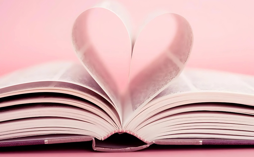 Open book with pages folded into a heart shape on a pink background, symbolizing Once Upon a Book Club's love for literature.