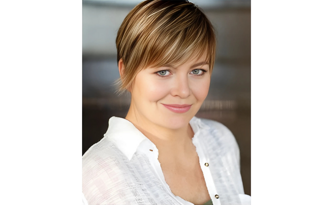 Lisa McMann, an author, with short blonde hair, blue eyes, and a white blouse, smiling softly against a neutral background.