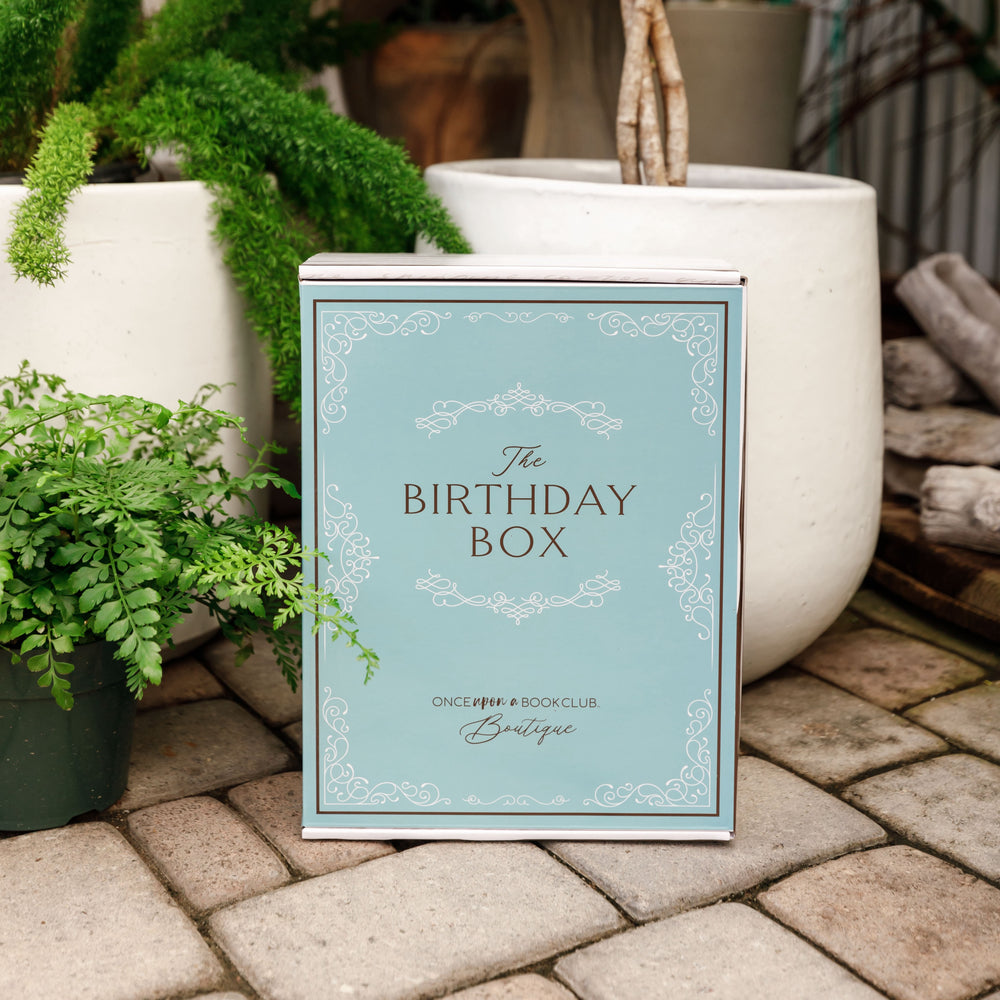 A robin's egg blue Birthday Box sits outdoors surrounded by greenery.