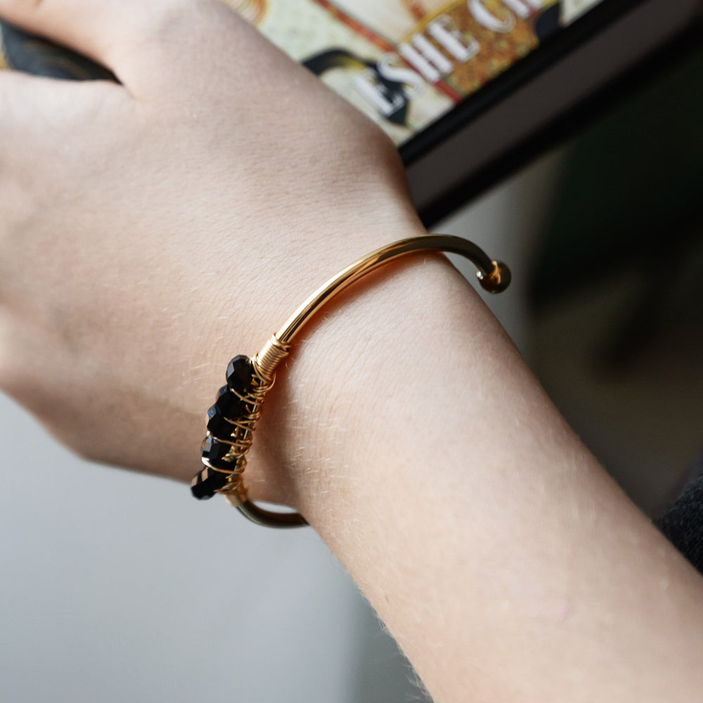 a gold cuff bracelet with black stones is worn on a woman's wrist.