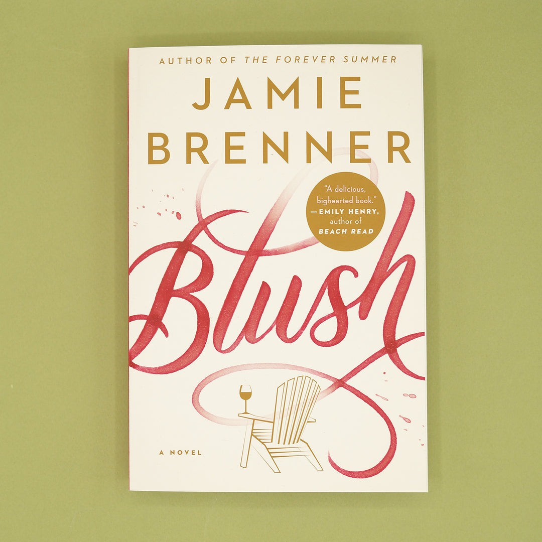 A paperback copy of Blush by Jamie Brenner sits on a green background.