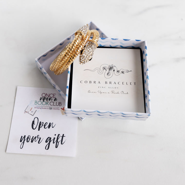 gold cobra bracelet with a crystal head and black eyes in an open box on an open your gift sticker