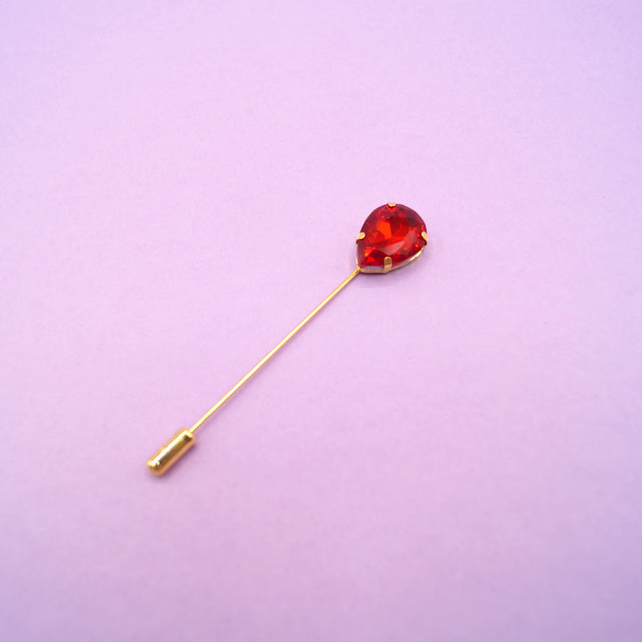 a red, teardrop gemstone straight pin brooch on a purple background.