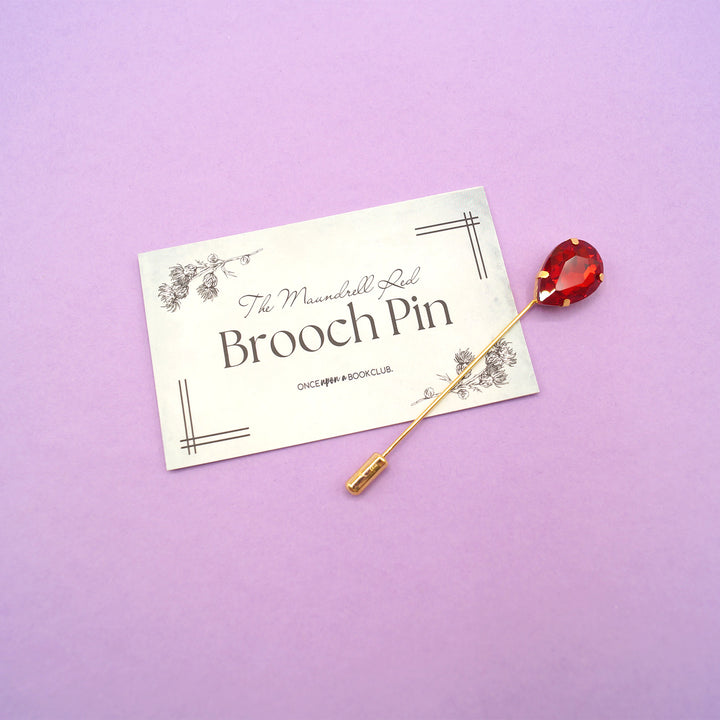 a red teardrop gemstone straight pin brooch sitting next to its matching tag.