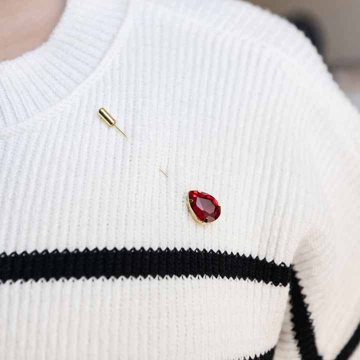 a red teardrop brooch straight pin pinned to a white striped sweater.