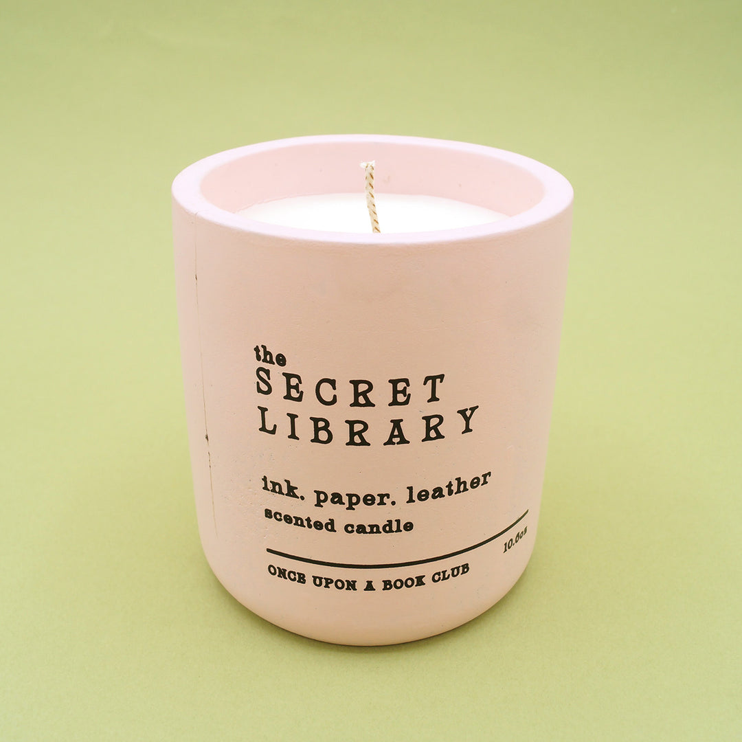 a gorgeous pink candle with vintage font "The Secret Library. ink paper leather. scented candle." on green background.