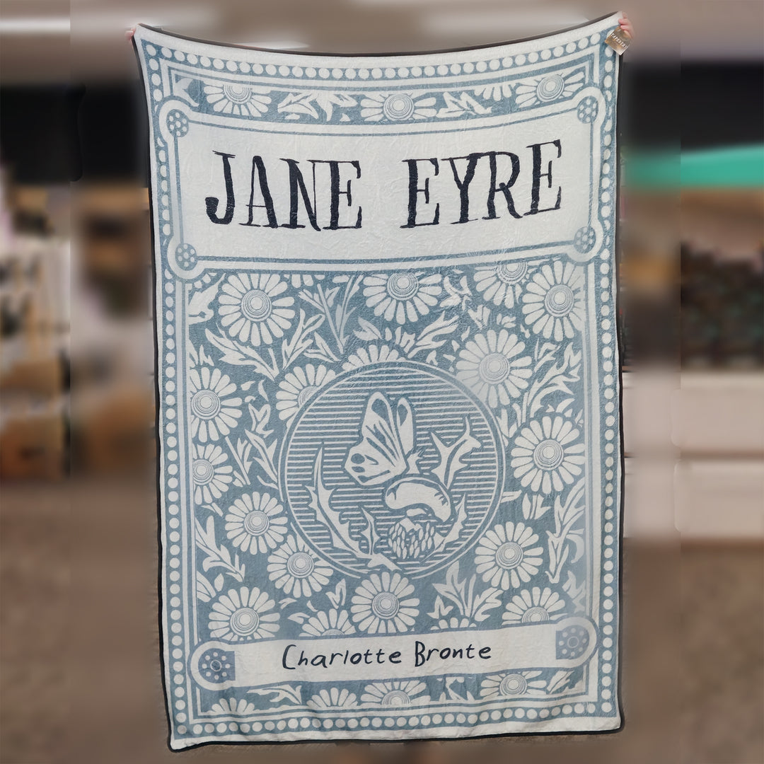 A large blanket featuring a green/blue background with flowers and butterflies and the words JANE EYRE by Charlotte Bronte written on the front.