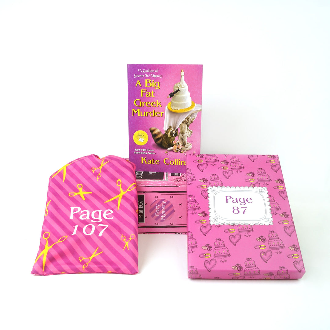 A mass market paperback edition of A Big Fat Greek Murder by Kate Collins sits on a pink book box surrounded by two wrapped gifts labeled with page numbers.