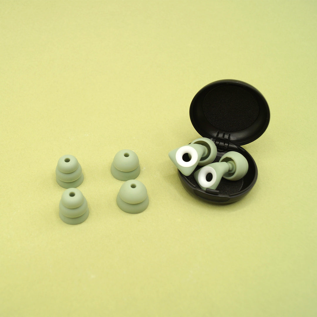 A set of green earplugs in a circular black case with four extra plugs of differing sizes next to it.