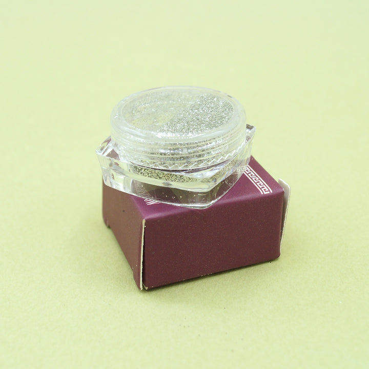 a small pot of silver glitter eyeshadow sits on a plum colored box.