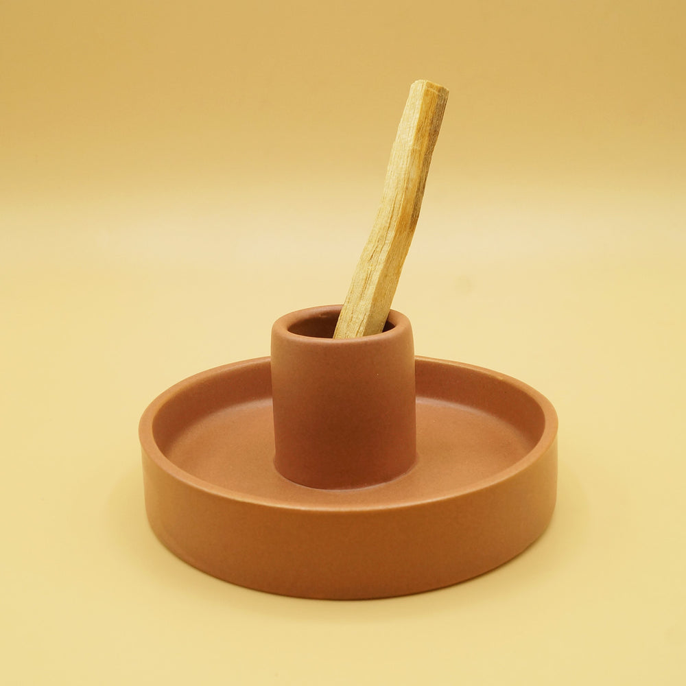 a round, clay colored dish with a 2" center piece holding the piece of palo santo wood.