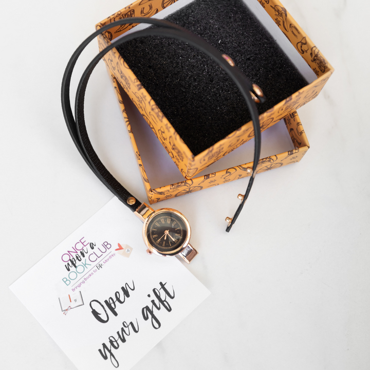 a black faux leather watch with rose gold accents sits next to an open top-lid box. An Open Your Gift sticky note sits next to the unwrapped item.