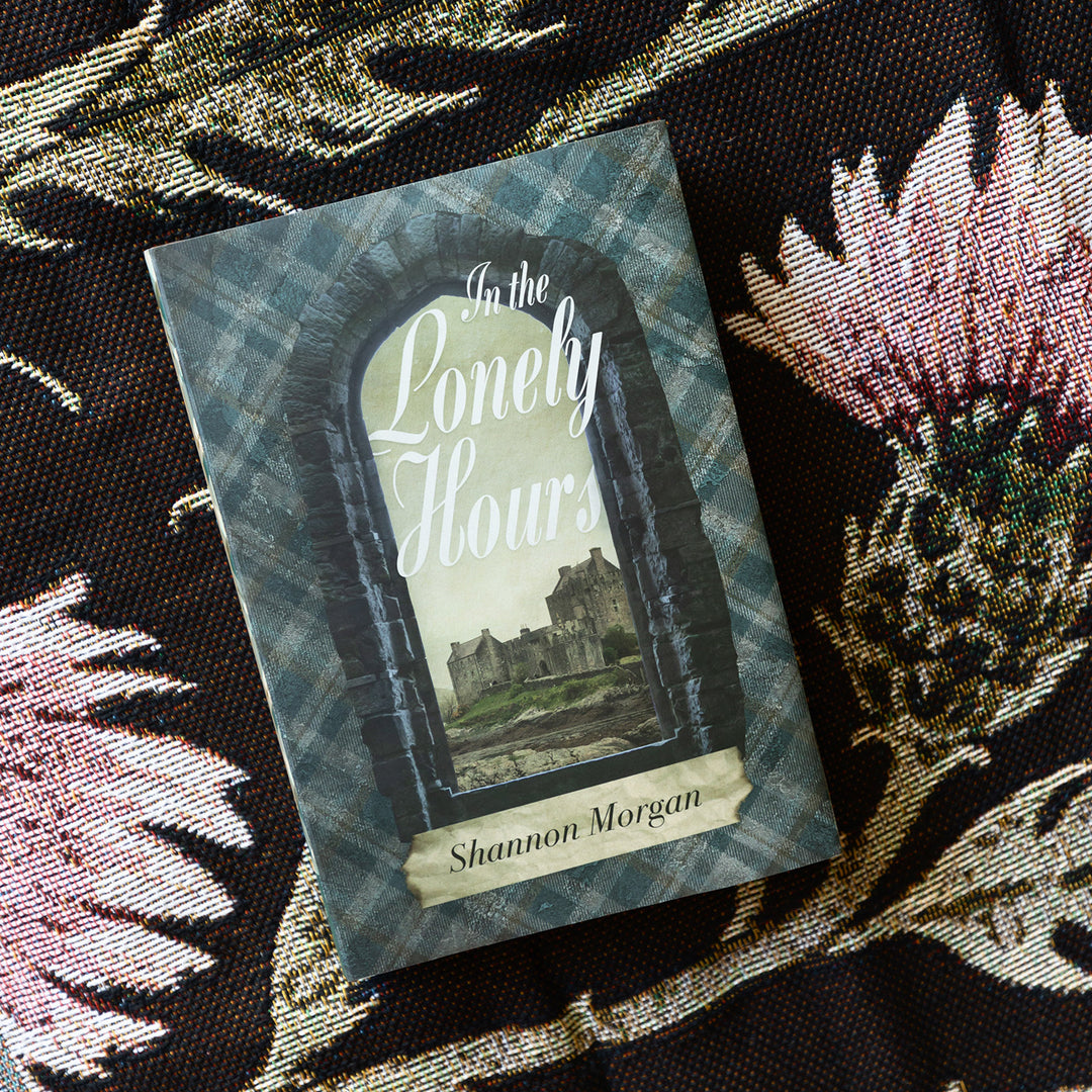 an exclusive, hardcover edition of In The Lonely Hours by Shannon Morgan sits on a woven thistle patterned blanket.