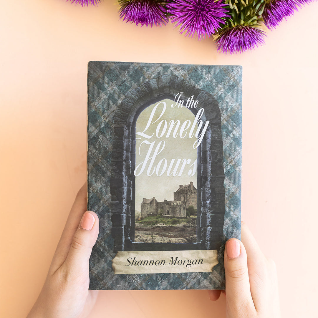 An exclusive, hardcover edition of In the Lonely Hours by Shannon Morgan showcasing the custom dust jacket featuring a stone arch overlooking a Scottish castle.