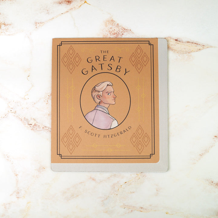 A light orange mouse pad meant to look like the book cover of The Great Gatsby featuring an illustration of Jay Gatsby in the center. On a pink marble background.