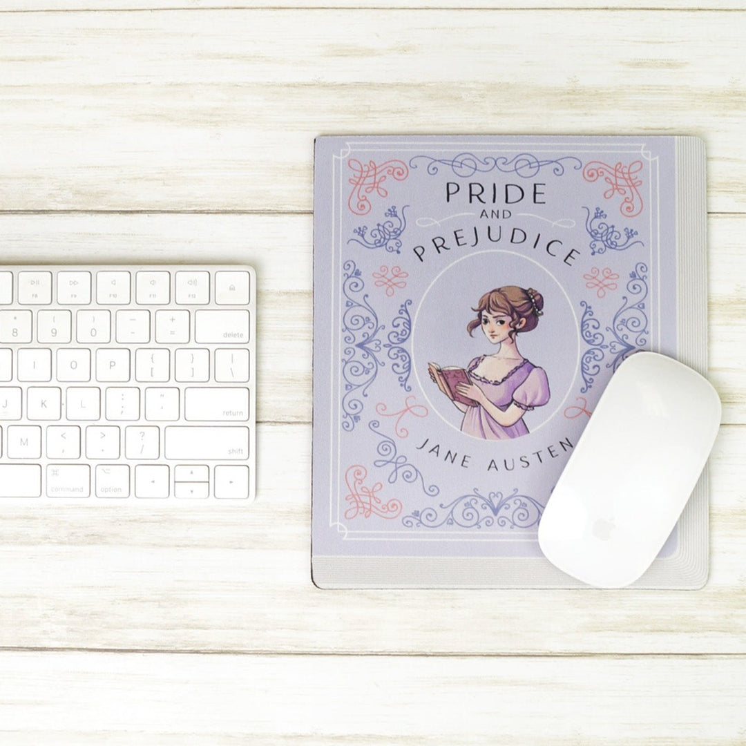 A light purple mouse pad meant to look like the book cover of Pride and Prejudice by Jane Austen featuring an illustration of Elizabeth Bennet in the center. The mousepad sits on a white wooden background with a keyboard to the left and a computer mouse on the bottom right of the mousepad.