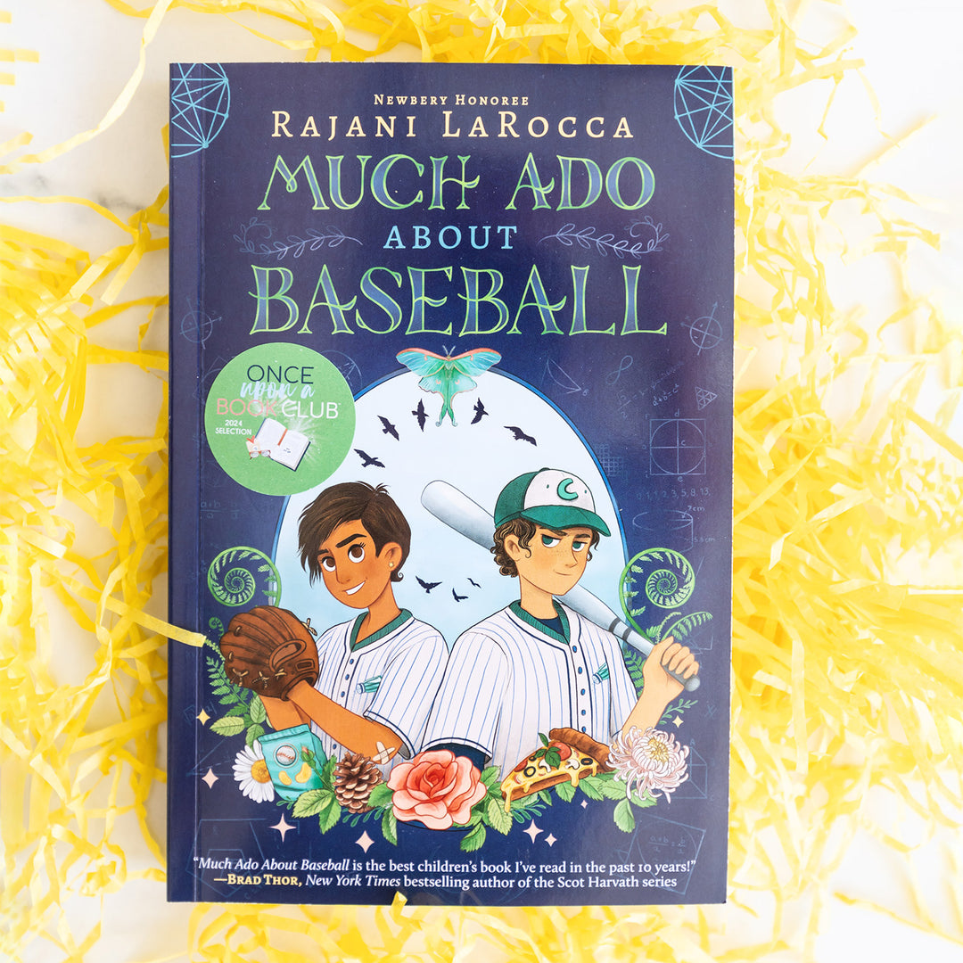 a paperback copy of Much Ado About Baseball by Rajani LaRocca on a bed of yellow shredded paper.