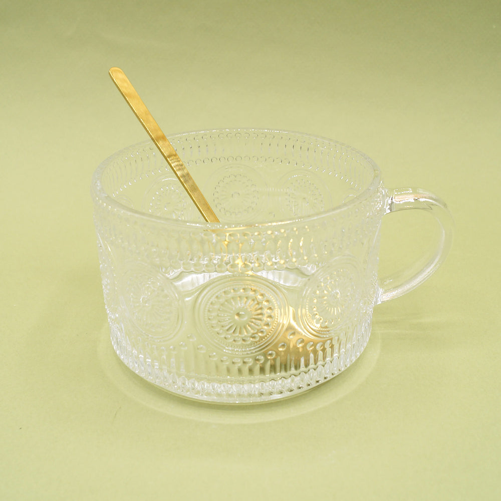 an oversized glass mug and a small gold spoon on a green background.