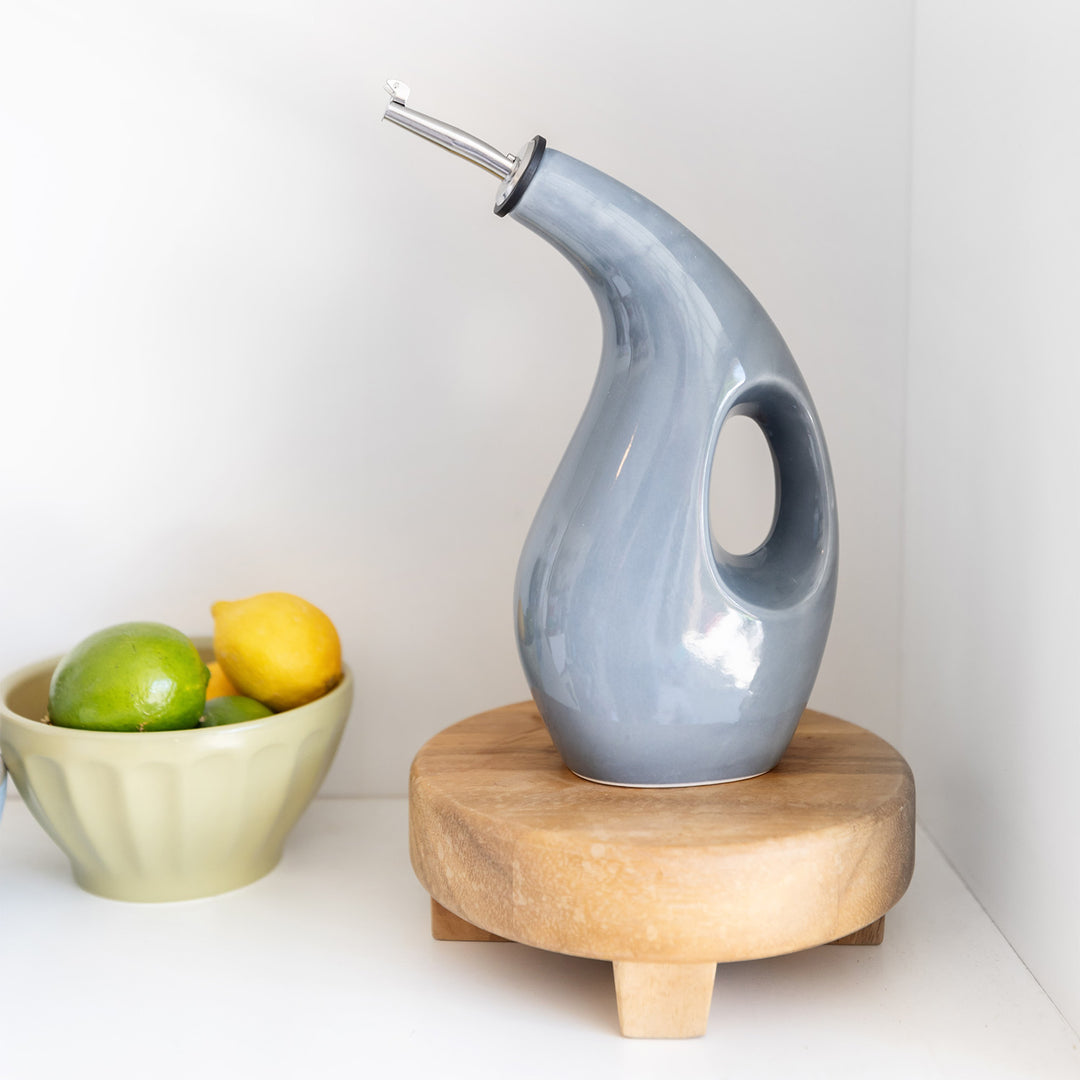 a gray-blue olive oil jug on a piece of wood next to a bowl of lemons and limes