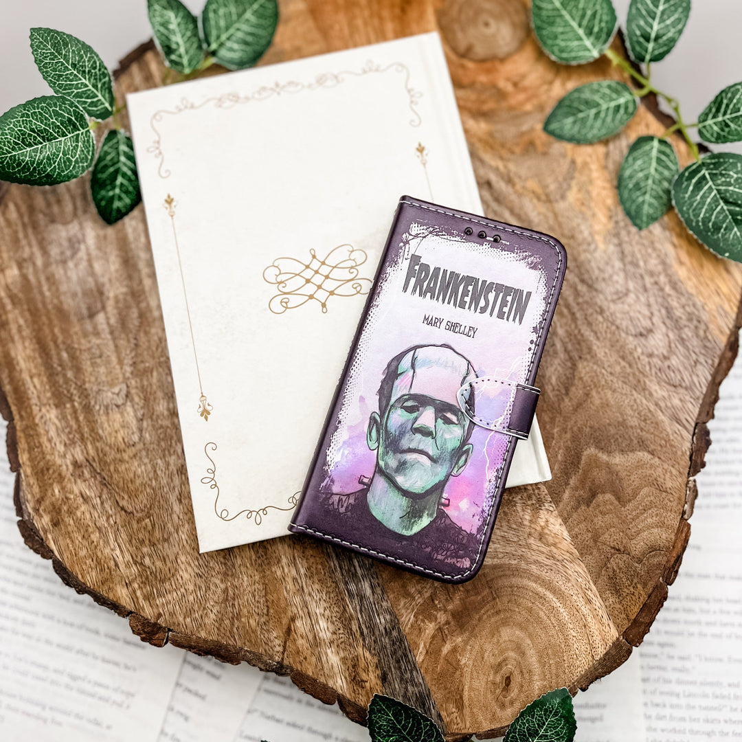 The front of a phone case inspired by Frankenstein by Mary Shelley. The phone case sits on a white book cover on a wood slice surrounded by greenery.