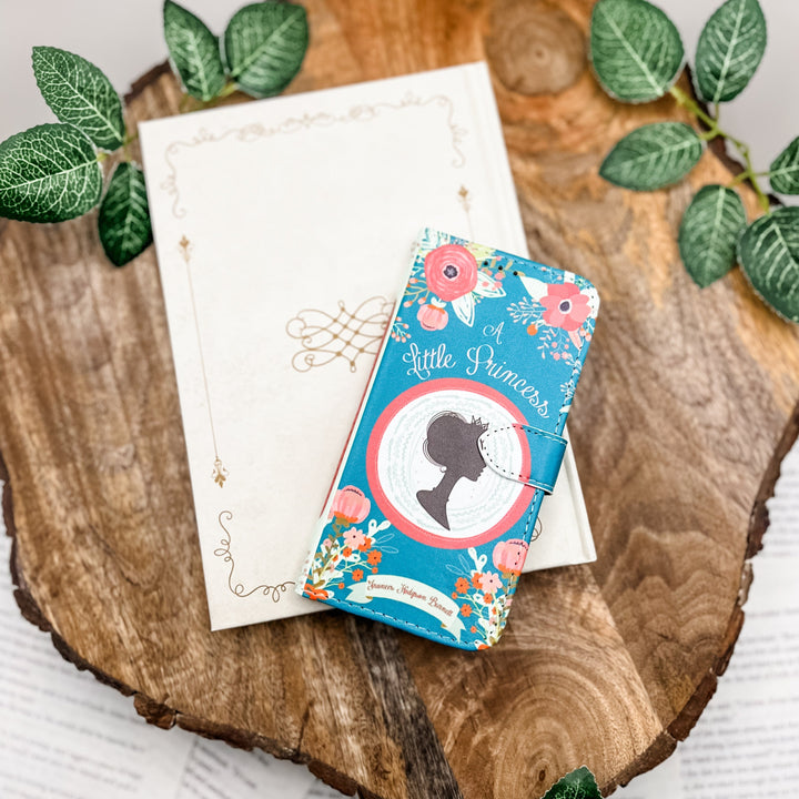The front cover of a phone case inspired by A Little Princess by Frances Hodgson Burnett on a wood slab with greenery.