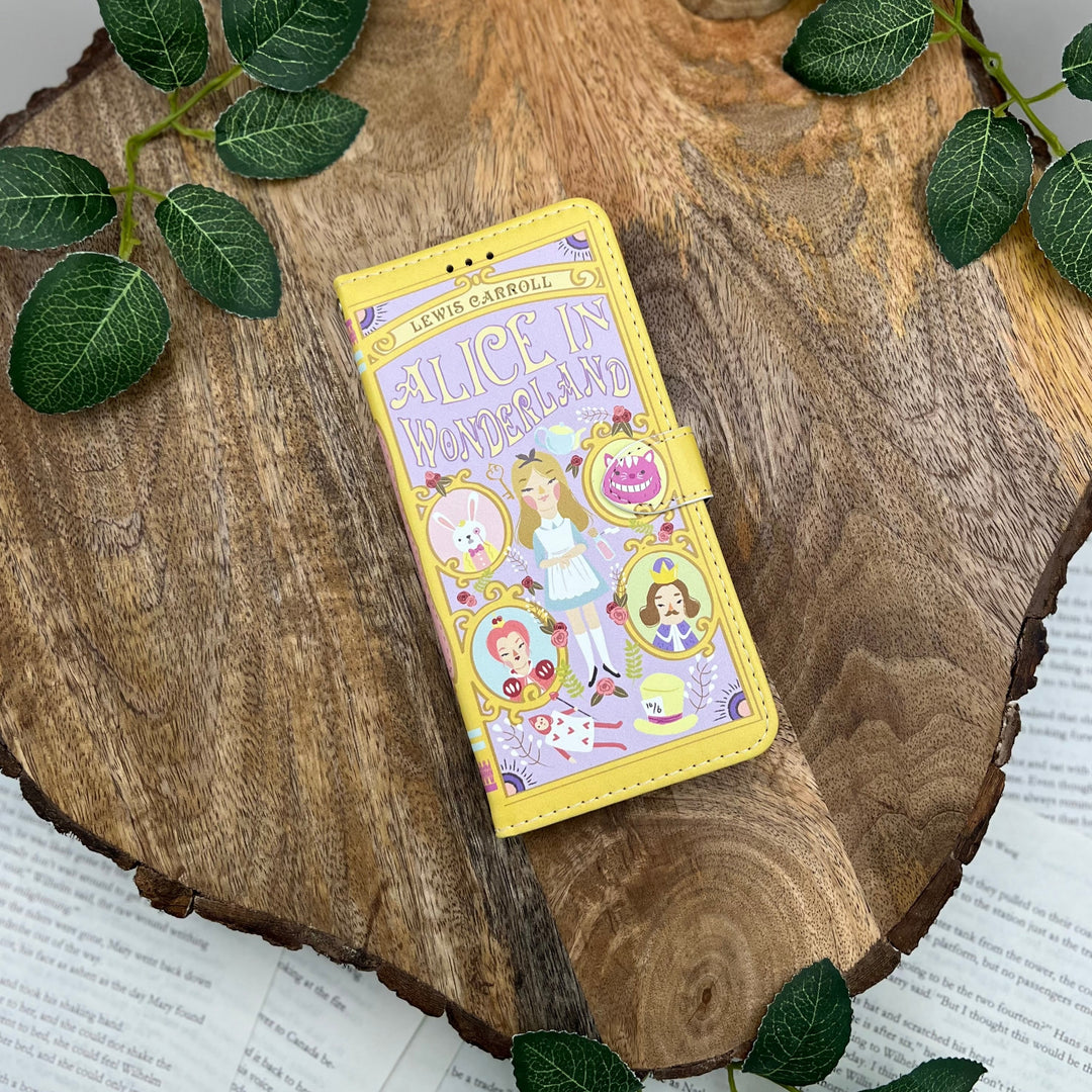 The front cover of a phone case inspired by Alice in Wonderland by Lewis Carroll. The phone case sits on a wood slice surrounded by greenery.