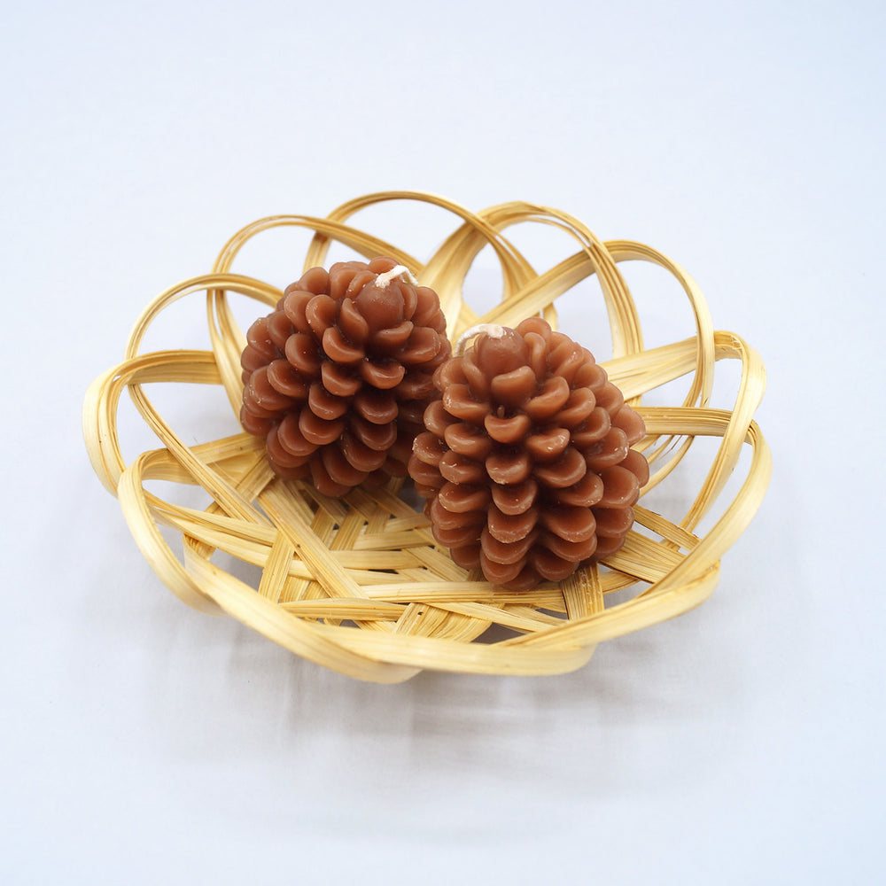 a set of two pinecone shaped candles and a small wicker basket.