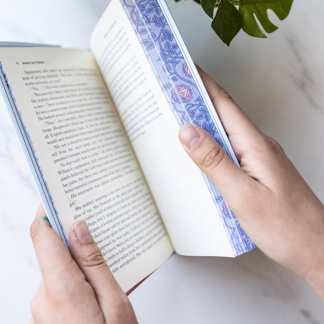 An exclusively designed hardcover copy of Sisters of Fortune by Anne Lee Huber as designed by the Once Upon a Book Club team. The sprayed edges are purple with pink and yellow details in a design by William Morris.