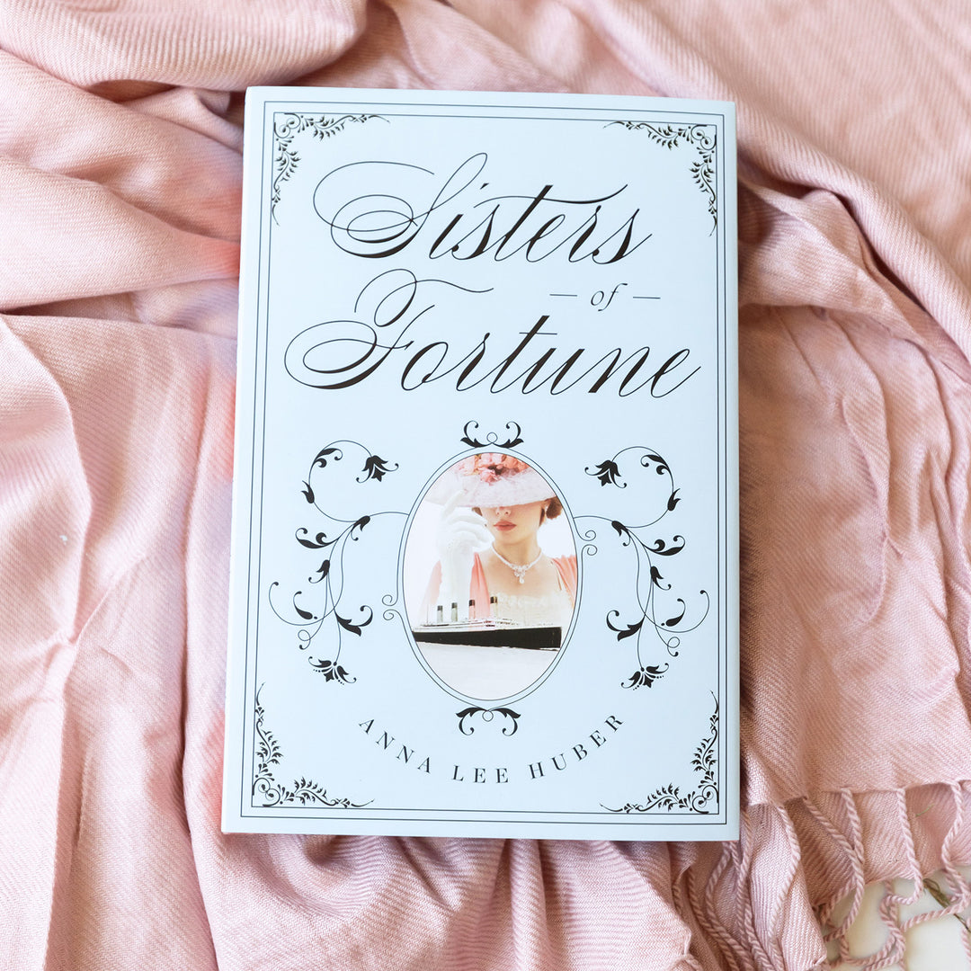 An exclusively designed hardcover copy of Sisters of Fortune by Anne Lee Huber as designed by the Once Upon a Book Club team. The dust jacket is light blue and features floral decor and an image of a white woman overlooking the Titanic.