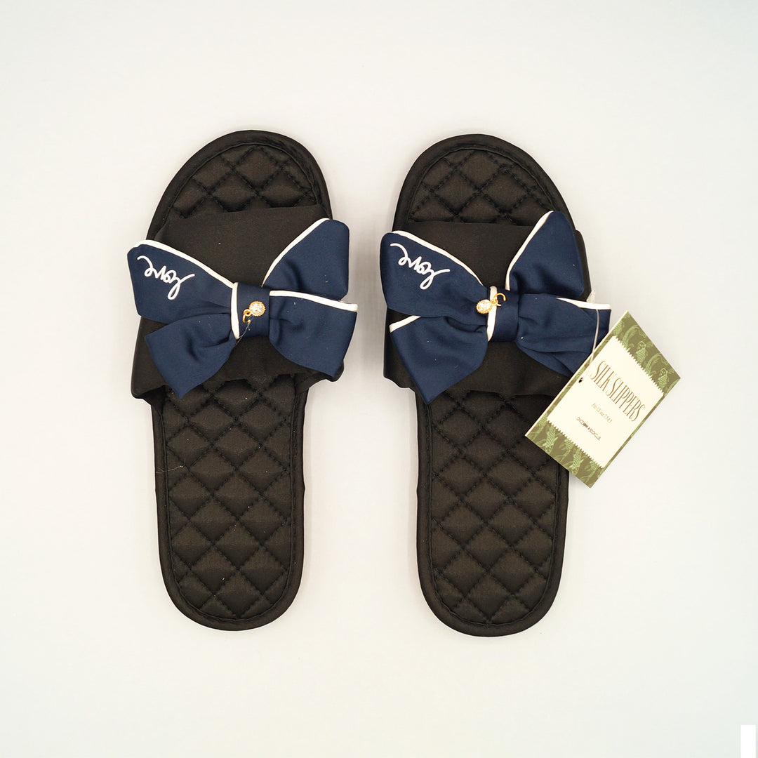 a pair of black and navy blue slippers with the word 'love' printed on the navy blue bow. a crystal hangs from the blue center bow. 