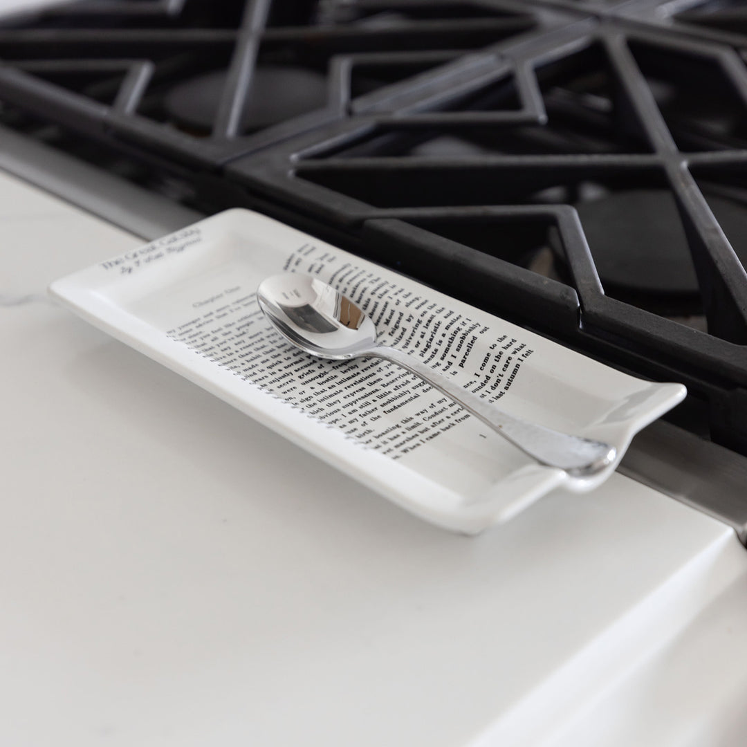 The ceramic spoon rest holding a spoon sits on a white countertop next to a gas range. Chapter One is legible across the top of the spoon rest.