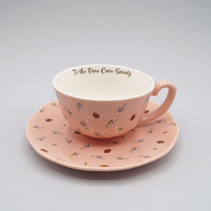 A pink floral and pine cone detailed teacup and saucer.