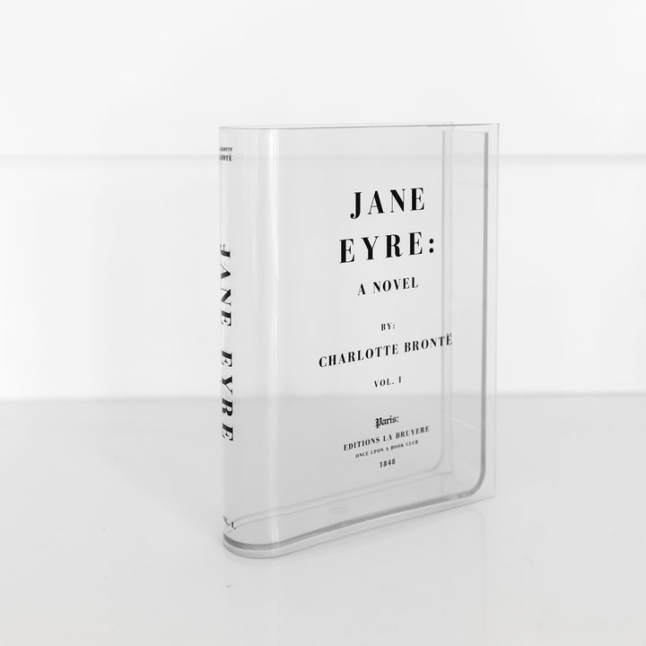 A clear acrylic book-shaped vase printed to look like a copy of Jane Eyre by Charlotte Bronte sits on a white surface. The spine is visible showing the book title.