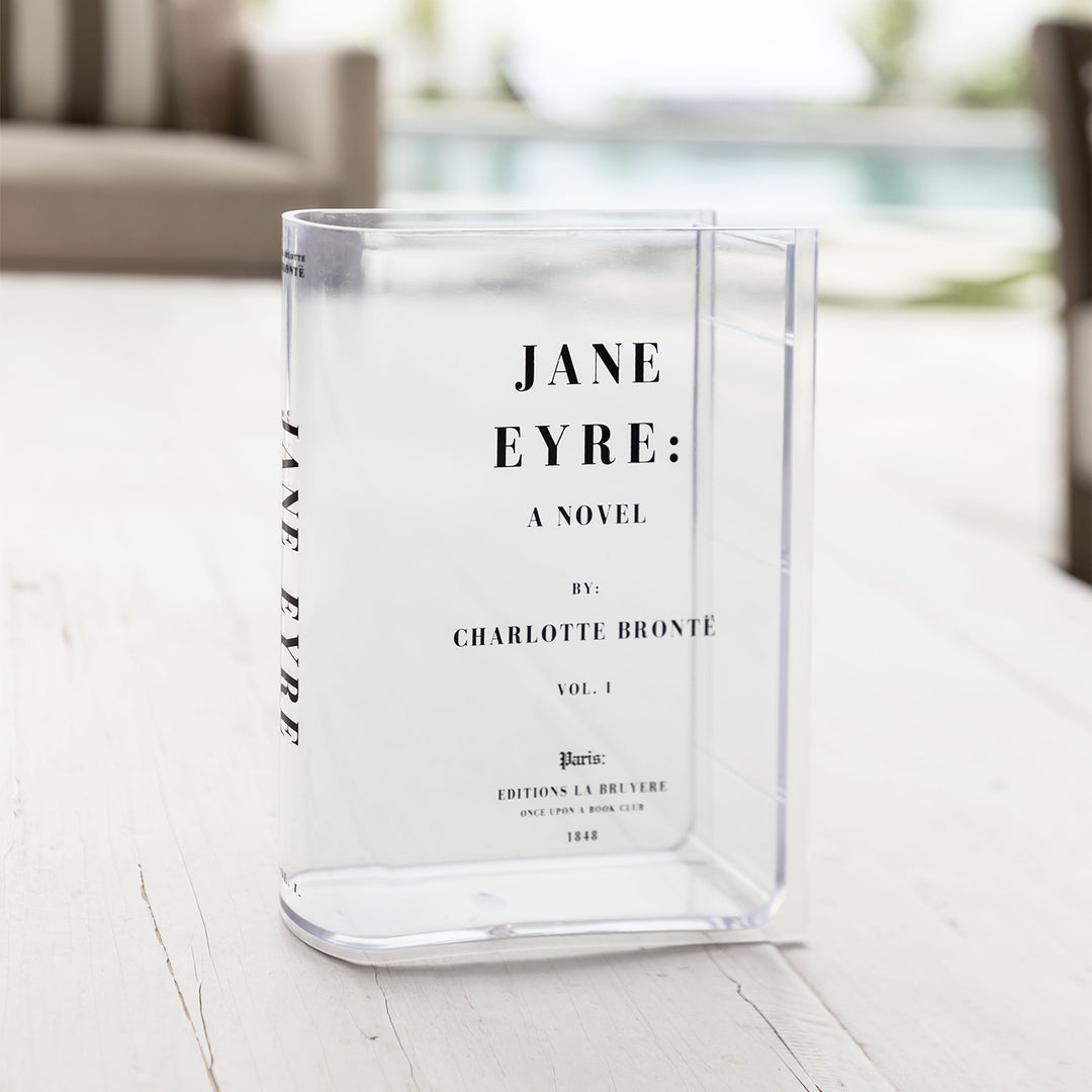A clear acrylic book-shaped vase printed to look like a copy of Jane Eyre by Charlotte Bronte sits outdoors.