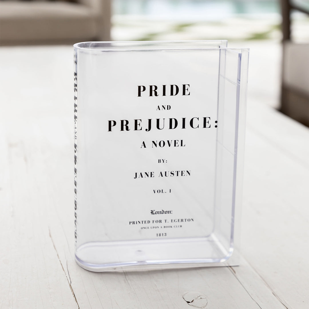 A clear acrylic book-shaped vase printed to look like a copy of Pride and Prejudice by Jane Austen sits outdoors.