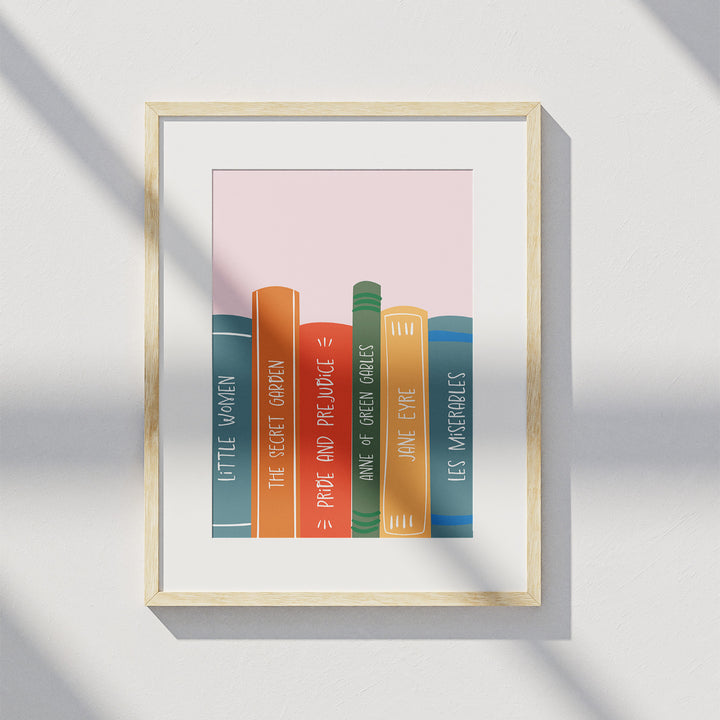 A matted wooden frame hangs on a white wall and displays the "Book Spines" art print. A shadow from a window is visible over the art print.