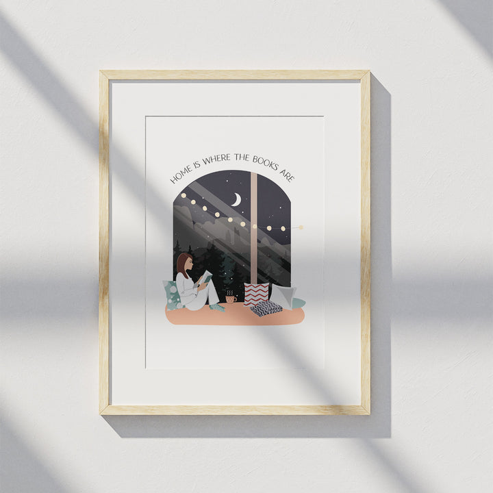 A matted wooden frame hangs on a white wall and displays the "Books Are Home" art print. A shadow from a window is visible over the art print.