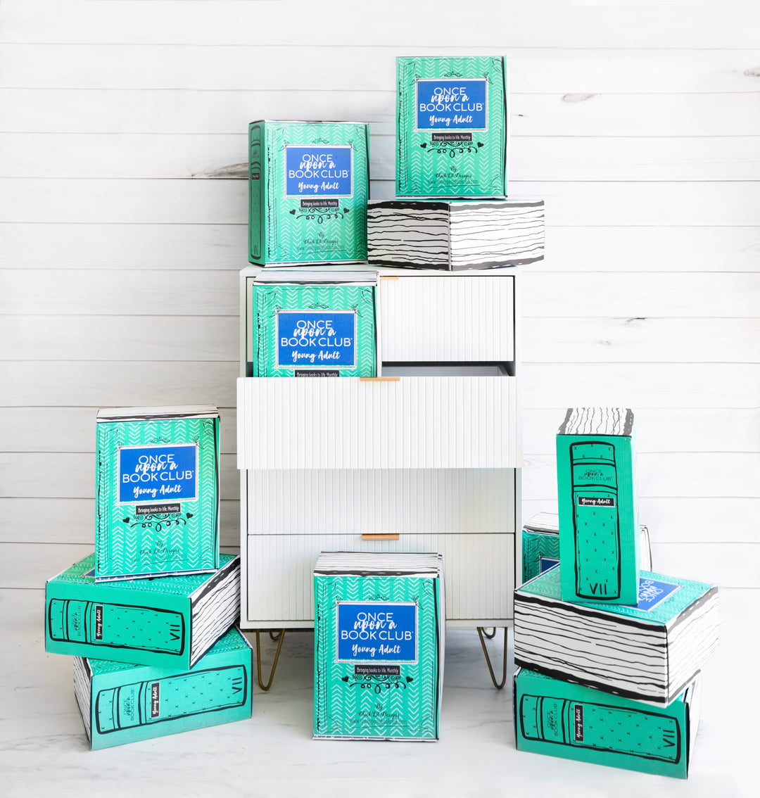 12 green Once Upon a Book Club Young Adult boxes sit on and around a chest of drawers